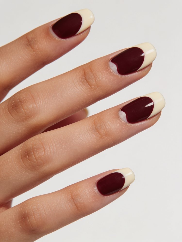 Medium oval nails in burgundy with a cream half moon at the base